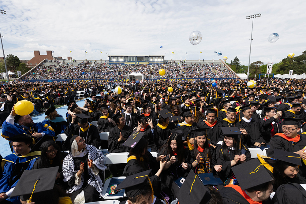 An overhead view of graduates and bleachers at a commencement ceremony.