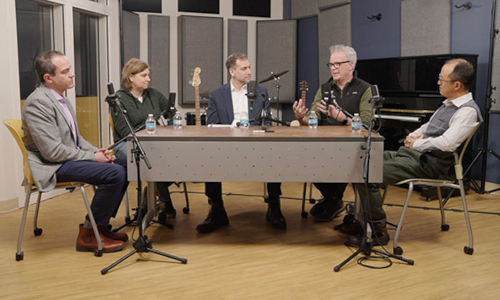 Five faculty conversing around a desk