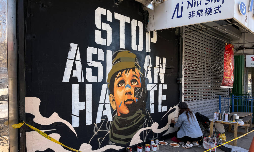 An assistant paints part of a mural by artist Dragon76 that reads "Stop Asian Hate" in Manhattan's Chinatown.